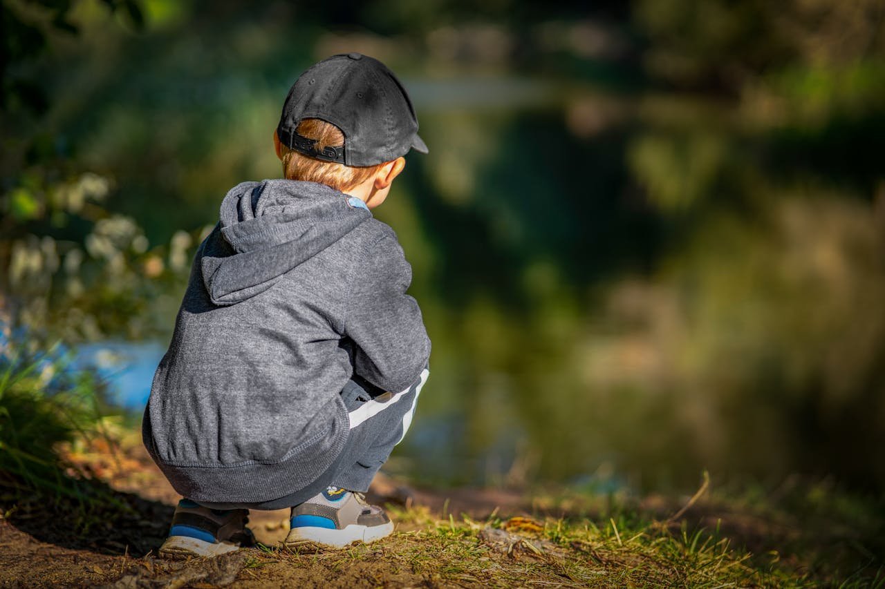 Crafting Captivating Headlines: Your awesome post title goes here A child in a hoodie squats by a tranquil forest lake, enjoying nature and sunlight.